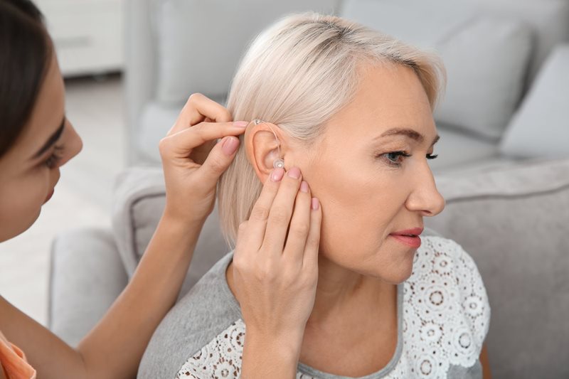 Frau wird ein Hinter-dem-Ohr Hörgerät eingesetzt